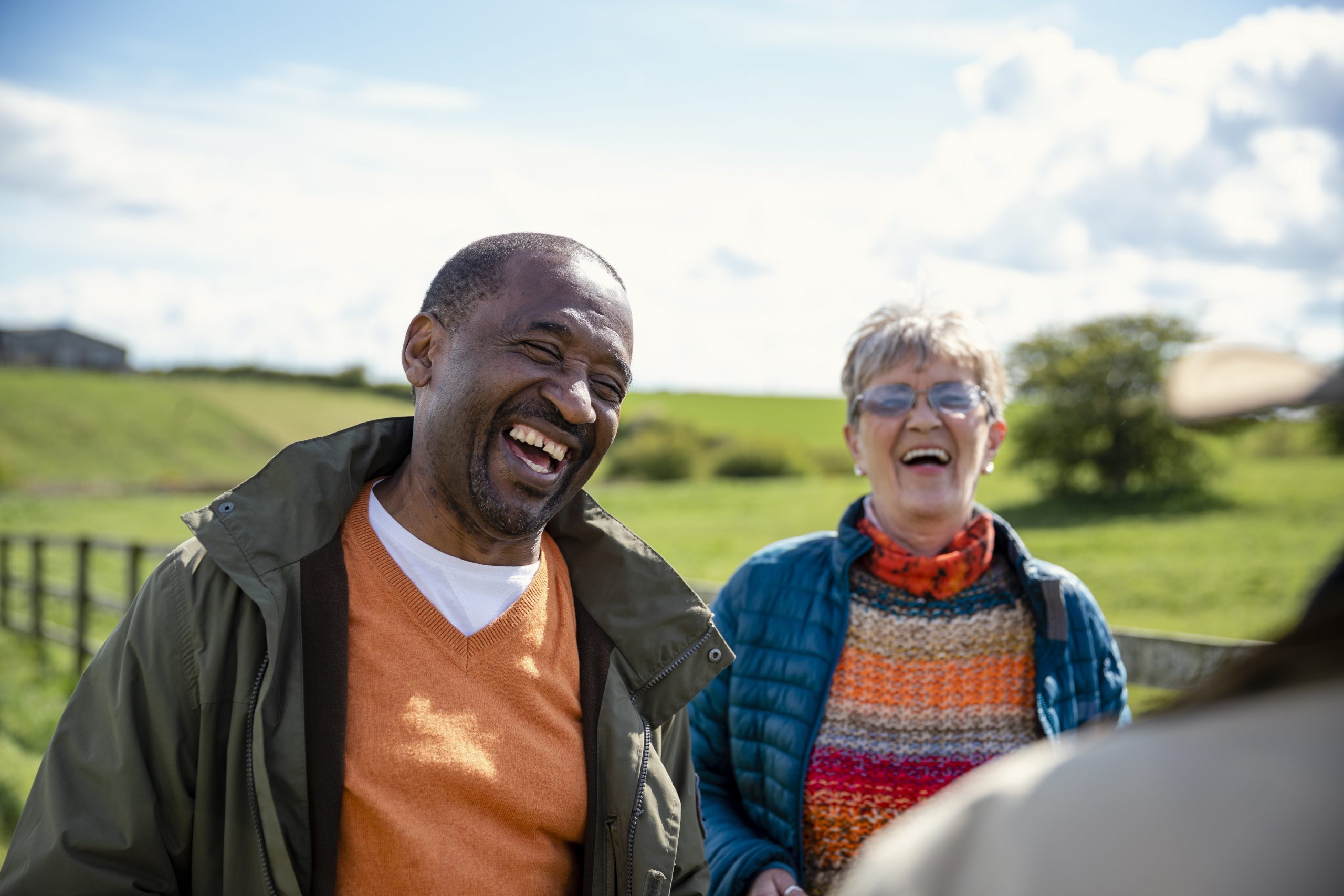 Senior friends standing in a field together while on staycation laughing and talking together. They are enjoying retirement together, being active in the North East of England.